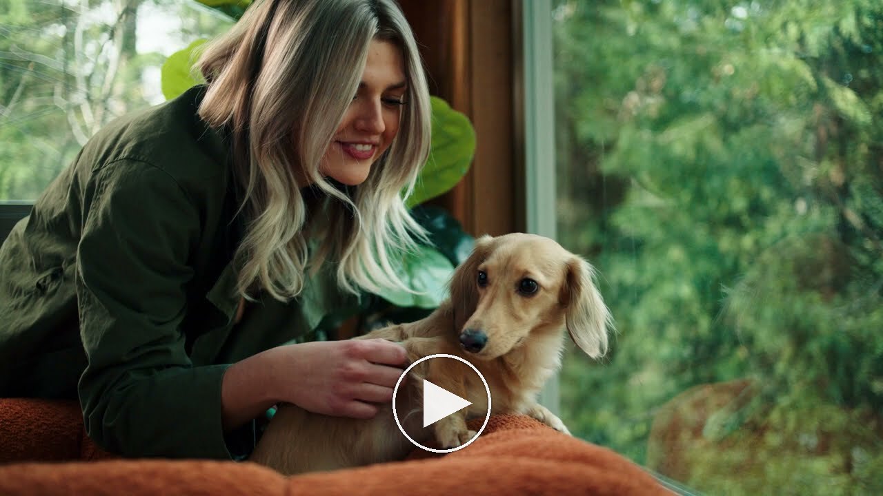 Kirsten, Miembro de Hannah, junto a una ventana con Maverick, su perro salchicha de pelo largo color crema